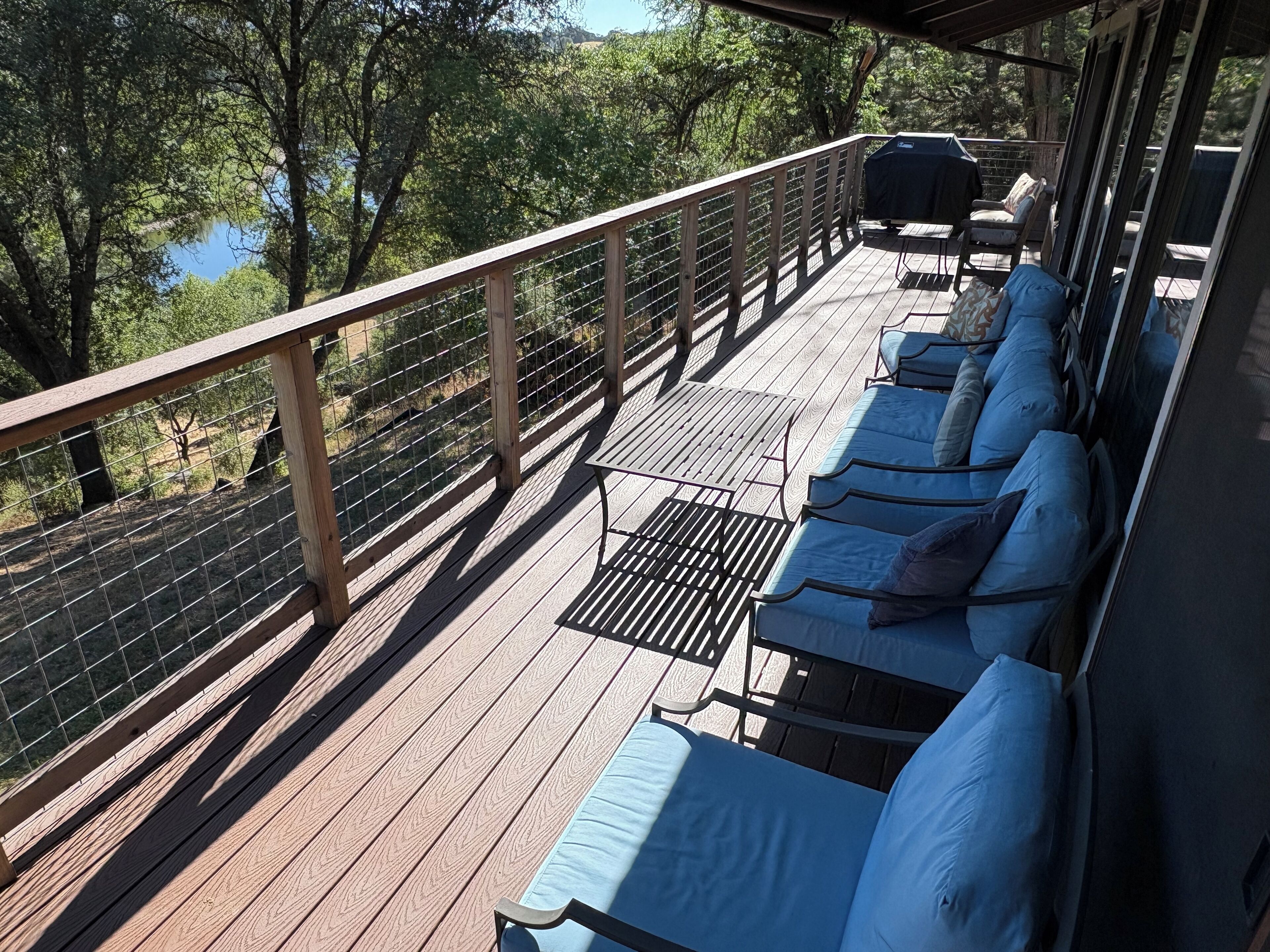 A wooden deck with blue cushioned seating and a grill, overlooking a wooded area.