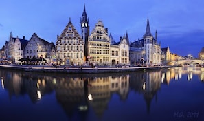 A historic European cityscape with a prominent clock tower and reflective water in the foreground. - Burgstraat 17 (Ghent)