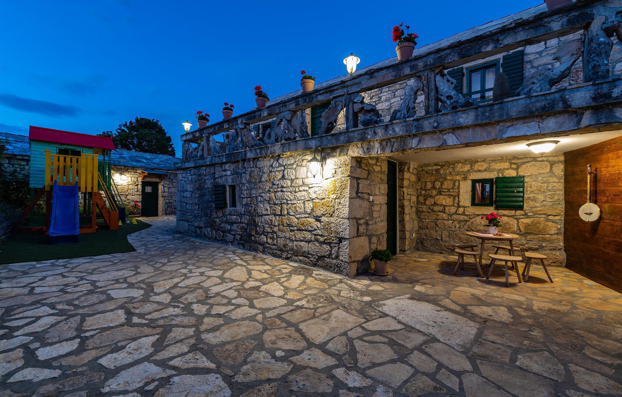 Un edificio in pietra con un balcone, un'area giochi e un tavolo con sedie.