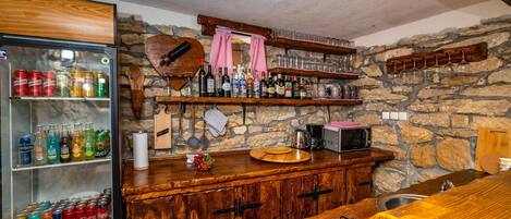 Un espace bar avec un mur en pierre, des étagères en bois remplies de bouteilles, un réfrigérateur contenant des boissons et un comptoir en bois avec un évier.