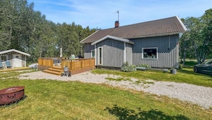 Eine kleine, eingeschossige Holzhütte mit einer Terrasse, umgeben von Bäumen.