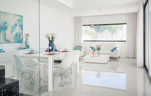 Relax in this stylish living room with a dining table for four, a sofa, and a large window offering a view of the surrounding greenery.