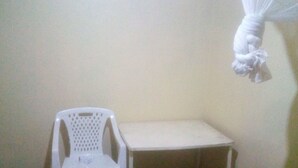 A small room with a white plastic chair, a small table, and a bed with a checkered bedspread. - Kiuu Guest House (Ruiru)