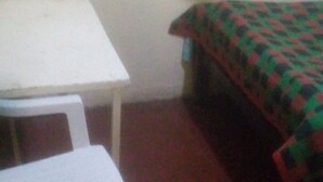 A small room with a white table and a chair, a bed with a green and red checkered bedspread, and a white wall. - Kiuu Guest House (Ruiru)