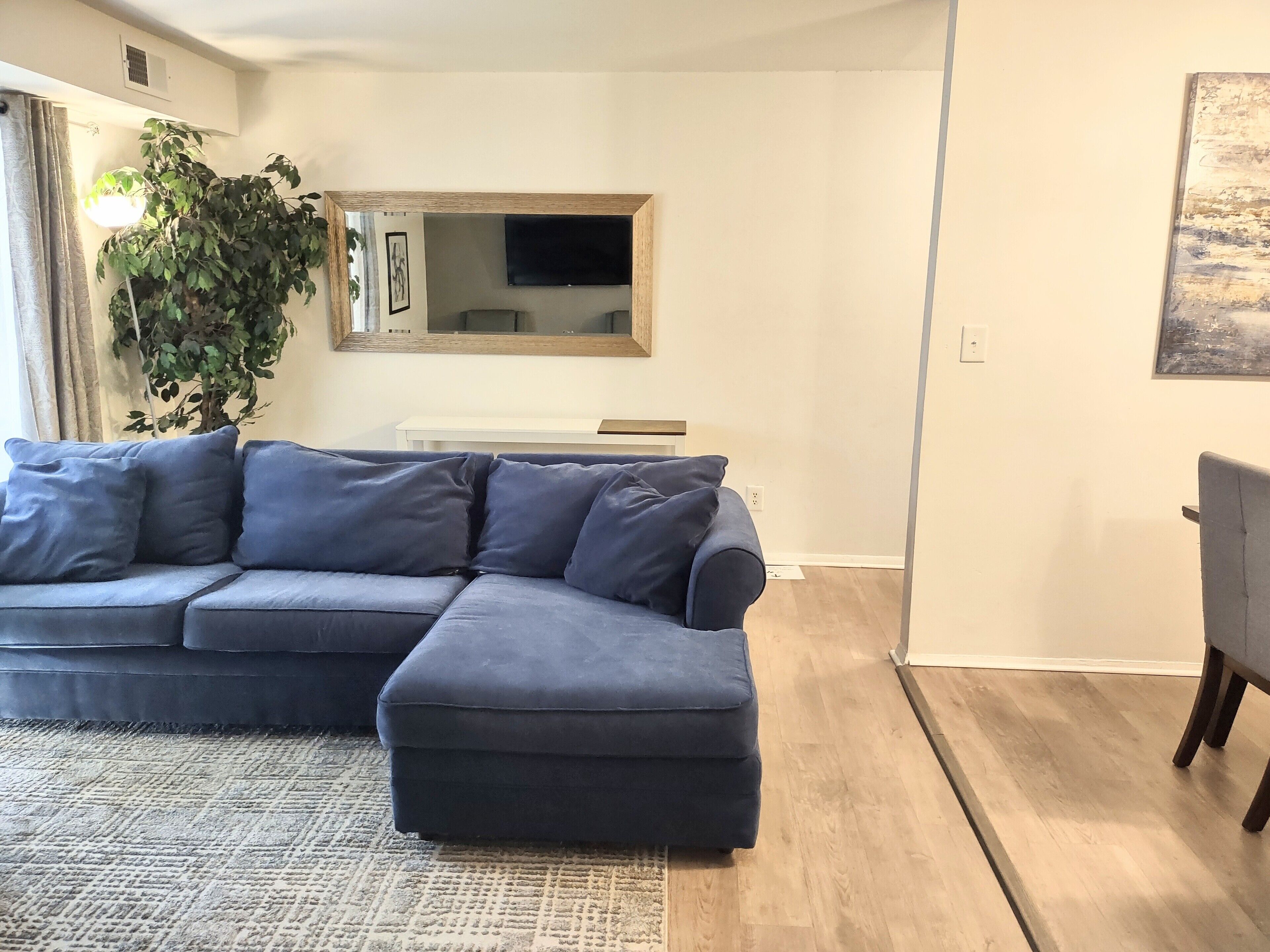 Una sala de estar con un sofá modular, una mesa de centro, un espejo grande y una planta en maceta.