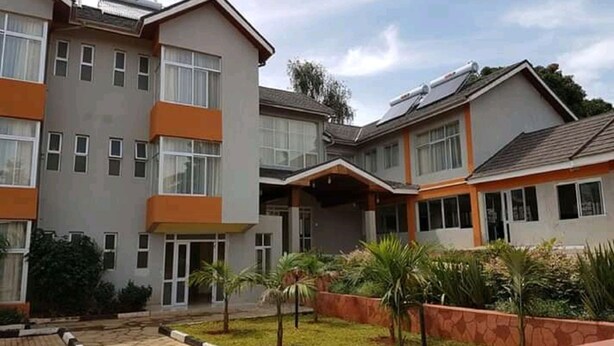 A multi-story residential building with a flat roof, a paved courtyard, and small palm trees. - Milimani Hotel (Kakamega)