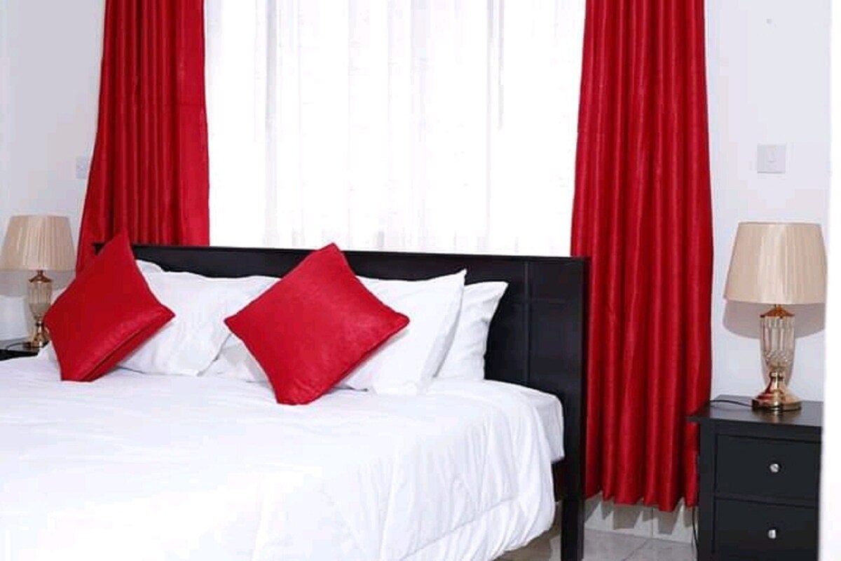 Una habitación de hotel con una cama, cortinas rojas, ropa de cama blanca y dos lámparas de noche.