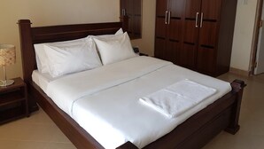 A neatly made bed with white linens, a wooden headboard, and a large wardrobe with two doors. - Milimani Hotel (Kakamega)
