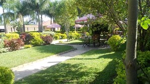 A well-maintained garden with a paved walkway leading to a seating area with tables and chairs. - Milimani Hotel (Kakamega)