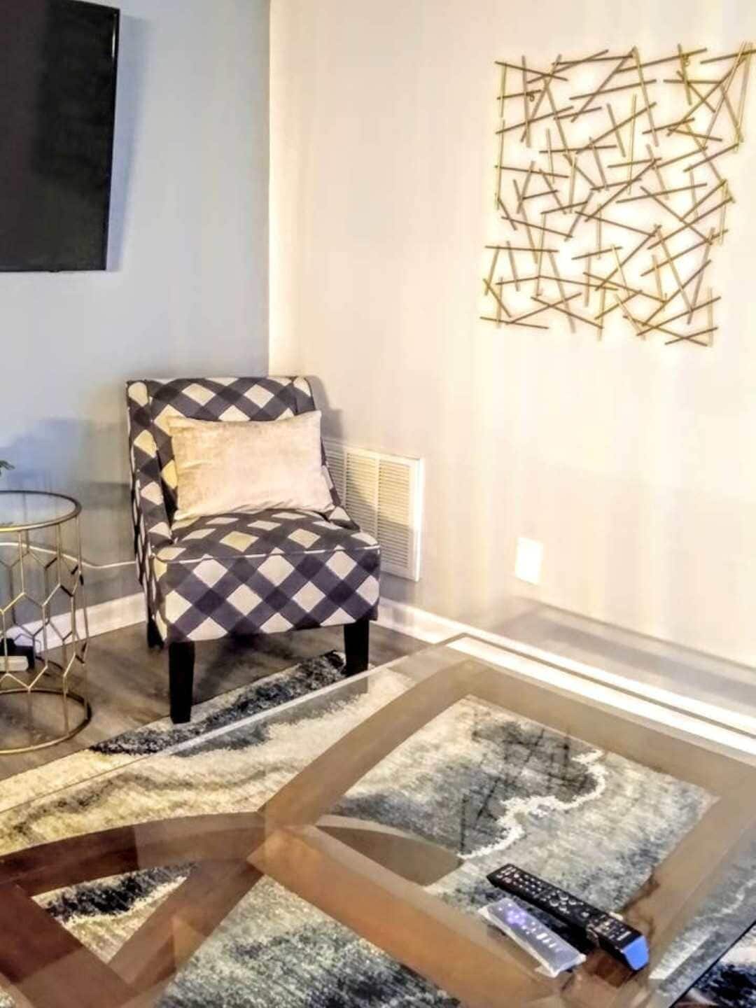 Un salon moderne avec un fauteuil à motifs, une table basse en verre et un élément décoratif mural.