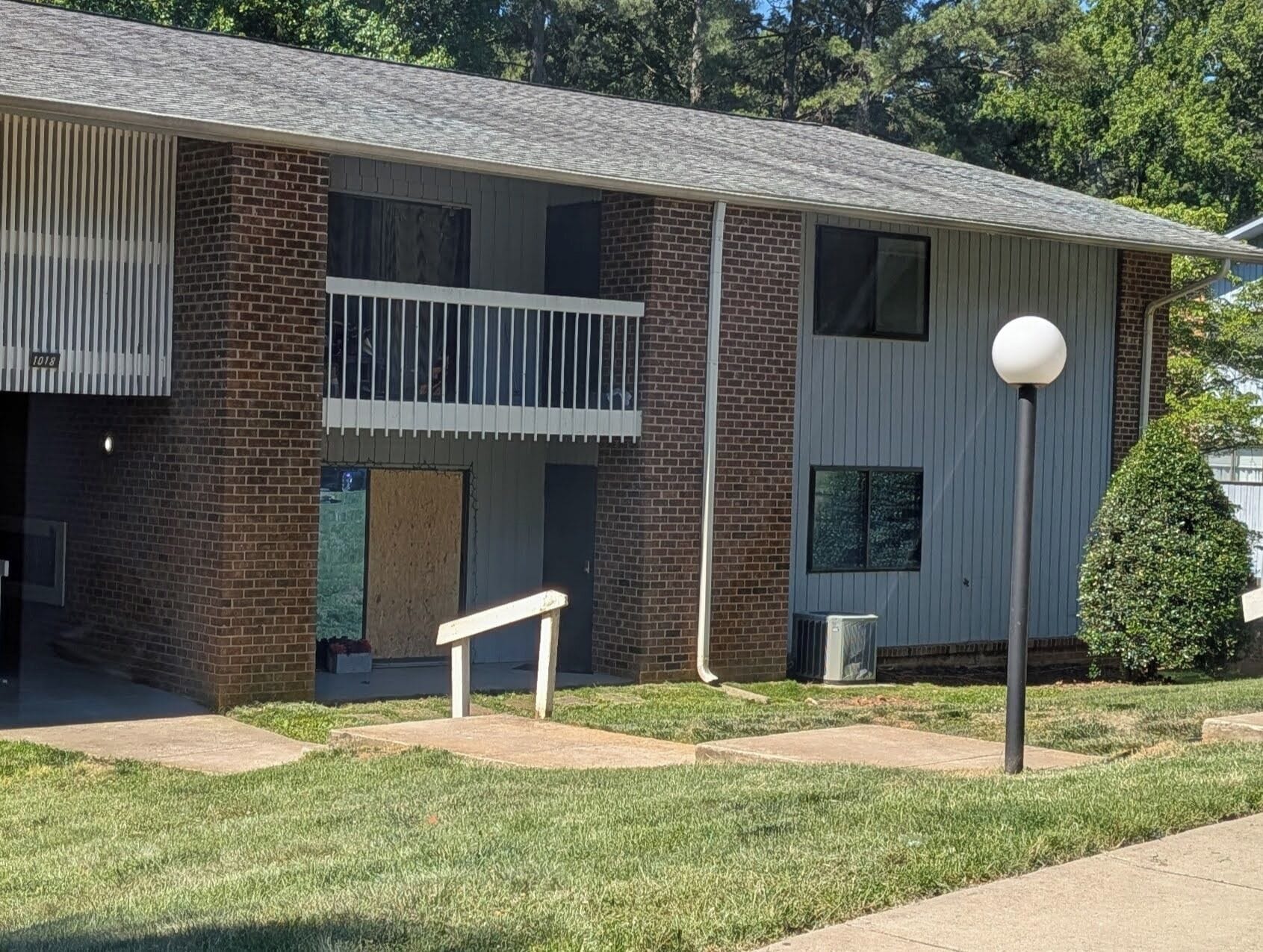 A two-story building with a brick facade, a balcony, and a small attached garage.