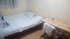 Une petite pièce, peu meublée, avec un lit simple, une petite table et une chaise.