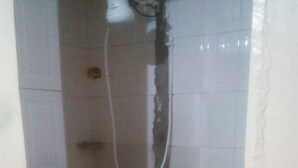 Un petit espace douche fermé, avec un lavabo rouge et une pomme de douche blanche.