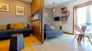 A modern living room with a sofa, a dining table with chairs, a TV mounted on the wall, and a bookshelf. - Flat Casino Beach Figueira da Foz - Moderno & Ótima Localização! (Figueira da Foz)