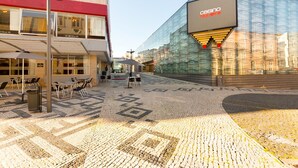An outdoor café area with tables and chairs, a modern building with a casino sign, and a patterned pavement. - Flat Casino Beach Figueira da Foz - Moderno & Ótima Localização! (Figueira da Foz)