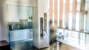 A modern kitchen with white cabinets, a microwave, and a glass partition. - Flat Casino Beach Figueira da Foz - Moderno & Ótima Localização! (Figueira da Foz)