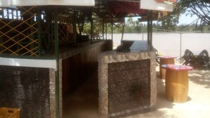 A covered outdoor seating area with a stone bench and a grill. - Rock Beach Resort (Ruiru)