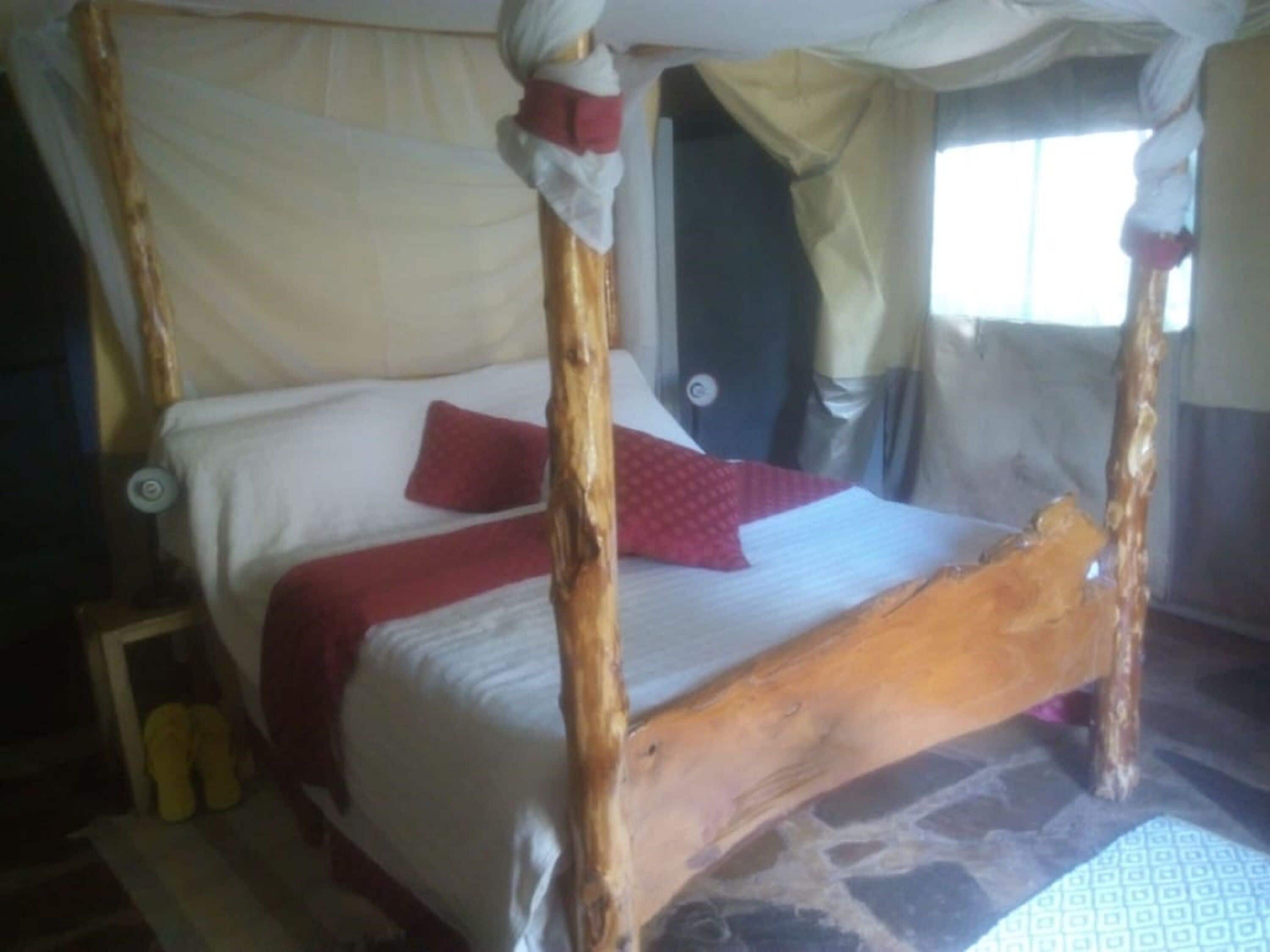 Een hemelbed met houten frame, wit beddengoed en een rood kussen.