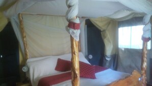 A four-poster bed with a canopy, a red pillow, and a wooden floor. - Rock Beach Resort (Ruiru)