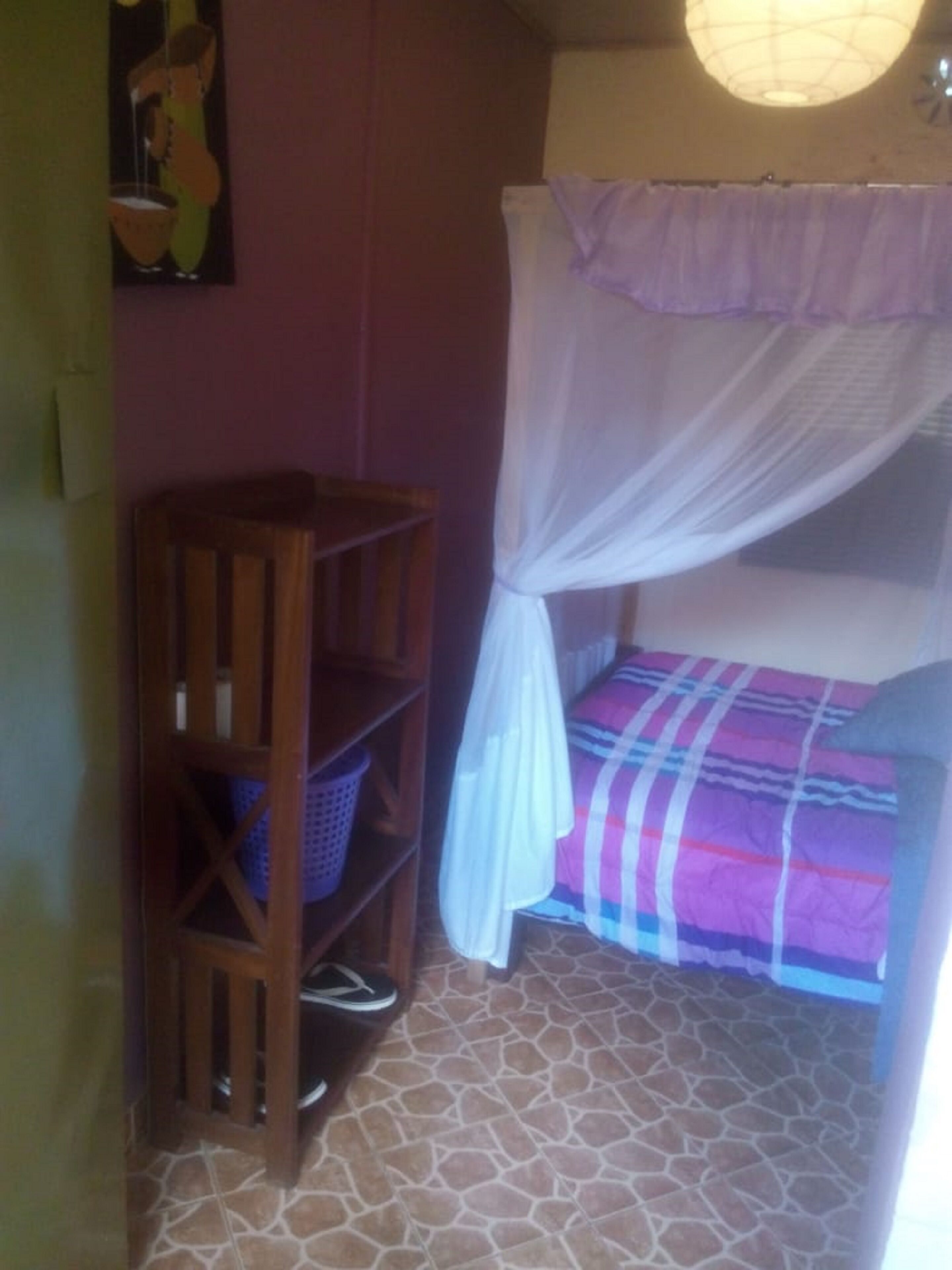 Une pièce comprenant un lit, une chaise en bois, une étagère et une moustiquaire.