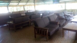 A covered seating area with multiple sofas and tables, a tiled floor, and a high ceiling. - Rock Beach Resort (Ruiru)