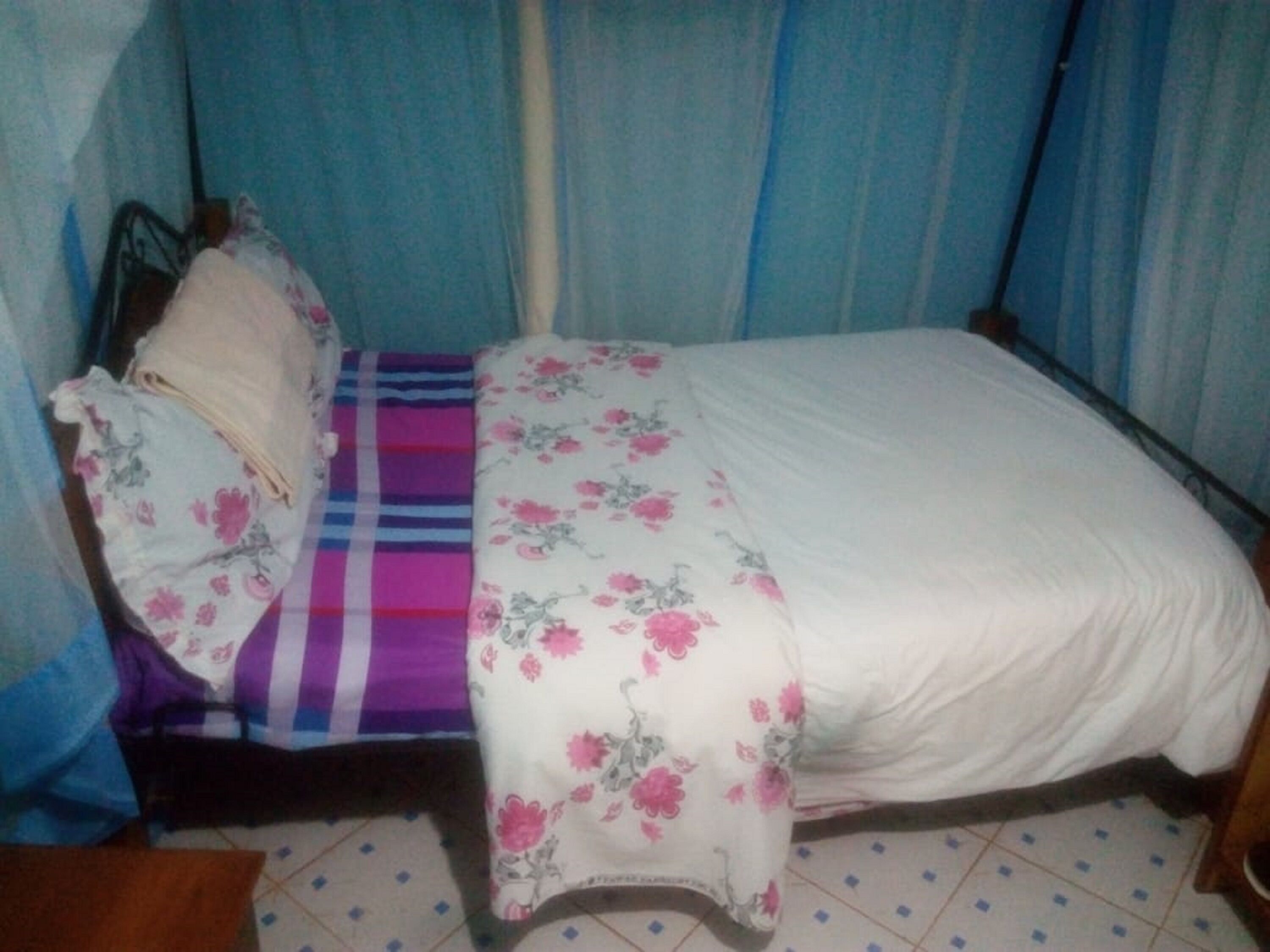 A single bed with a floral bedspread and a striped blanket, a pillow, and a headboard.