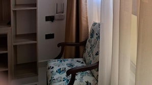 A room with a wooden bookshelf, a floral-patterned chair, and a window with sheer curtains. - Sailors Hotel (Mlolongo)