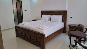 A spacious bedroom with a large bed, a wooden headboard, a bedside table, and a chair. - Sailors Hotel (Mlolongo)