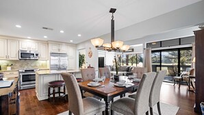 A modern kitchen with built-in appliances, a dining area with a wooden table and chairs, and large windows offering a view of the outdoors. - Daze Off! Stunning end unit villa  with two bedrooms and loft. Two King Beds! (Hilton Head Island)