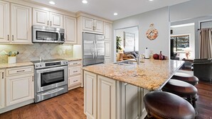 A modern kitchen with stainless steel appliances, a granite countertop, and a bar area with stools. - Daze Off! Stunning end unit villa  with two bedrooms and loft. Two King Beds! (Hilton Head Island)