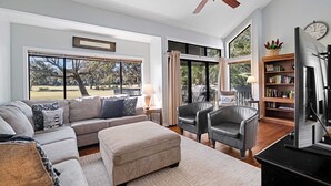 A spacious living room with a sectional sofa, two leather armchairs, a fireplace, and a large window offering a view of the outdoors. - Daze Off! Stunning end unit villa  with two bedrooms and loft. Two King Beds! (Hilton Head Island)