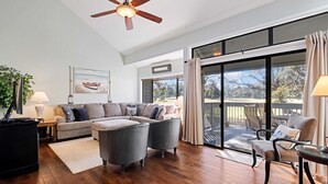 A spacious living room with a sectional sofa, a ceiling fan, and a large sliding glass door leading to an outdoor patio. - Daze Off! Stunning end unit villa  with two bedrooms and loft. Two King Beds! (Hilton Head Island)