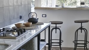 A modern kitchen with a gas stove, two bar stools, and a window with a view of greenery.