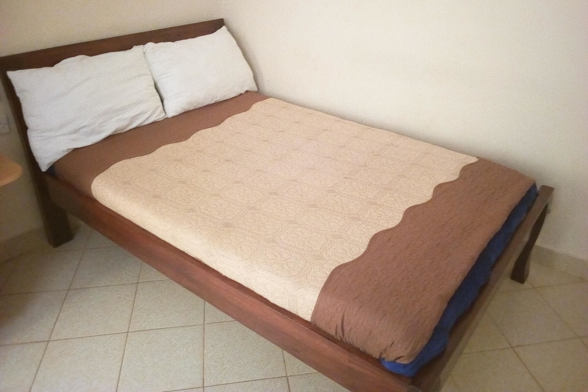 A single bed with a wooden frame, a beige and brown blanket, and two white pillows.