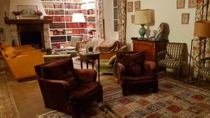 A cozy living room with a fireplace, a bookshelf, and a variety of seating options including armchairs and a sofa. - Charming house in the forest of Fontainebleau in a village of character (Recloses)