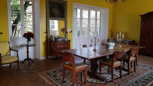 A dining room with a wooden table and chairs, a yellow wall, and a large window. - Charming house in the forest of Fontainebleau in a village of character (Recloses)