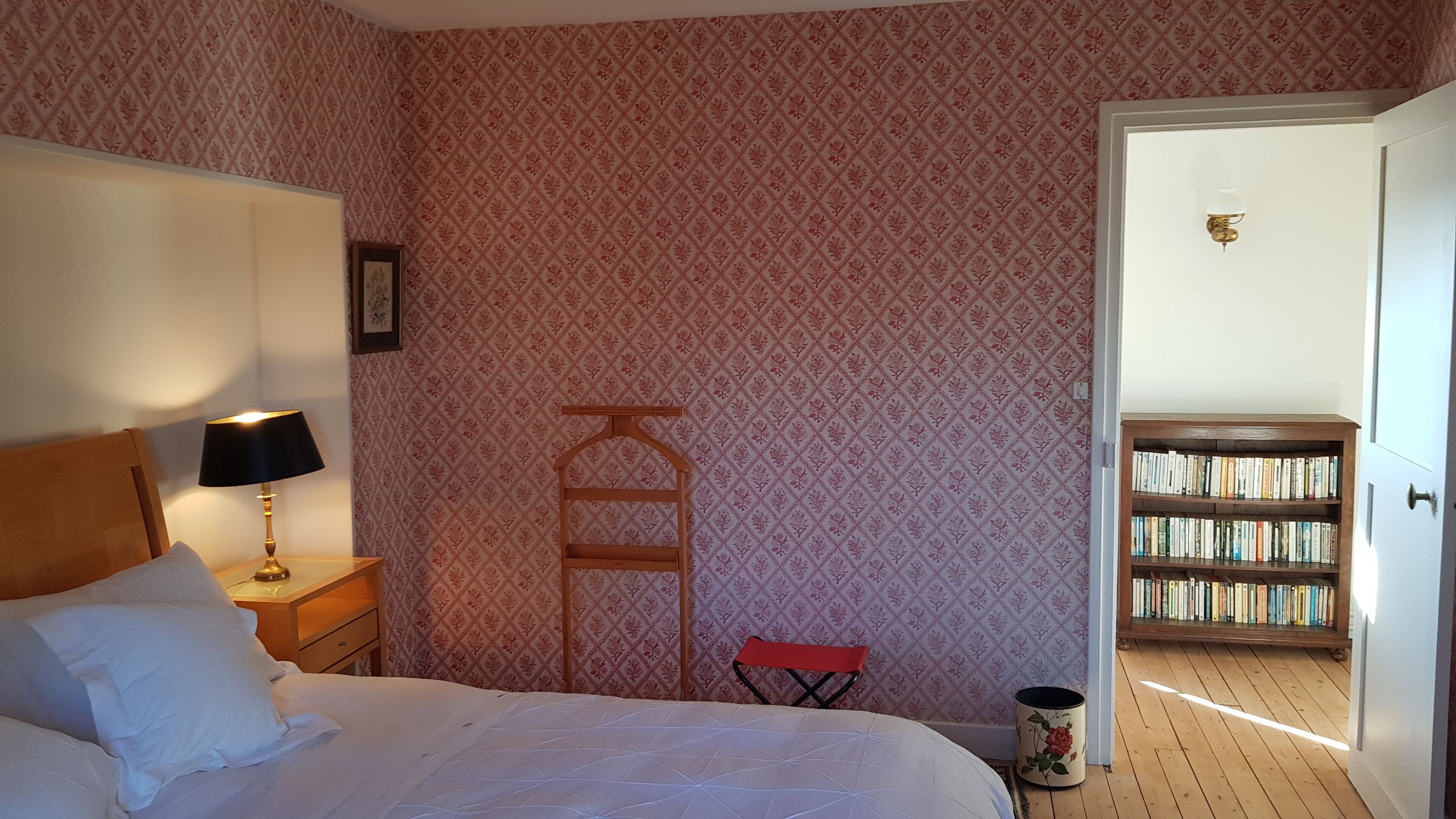 Une chambre à coucher comprenant un lit, une table de chevet, une lampe et une bibliothèque située dans la pièce adjacente.