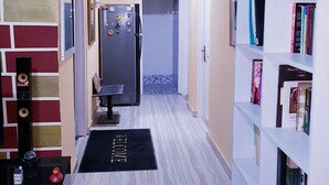 Un couloir avec un réfrigérateur noir, une bibliothèque, un tableau encadré et un tapis noir orné de motifs textuels.