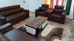 Un salon avec un canapé en cuir marron, deux fauteuils inclinables, une table basse en bois et un tapis à motifs.