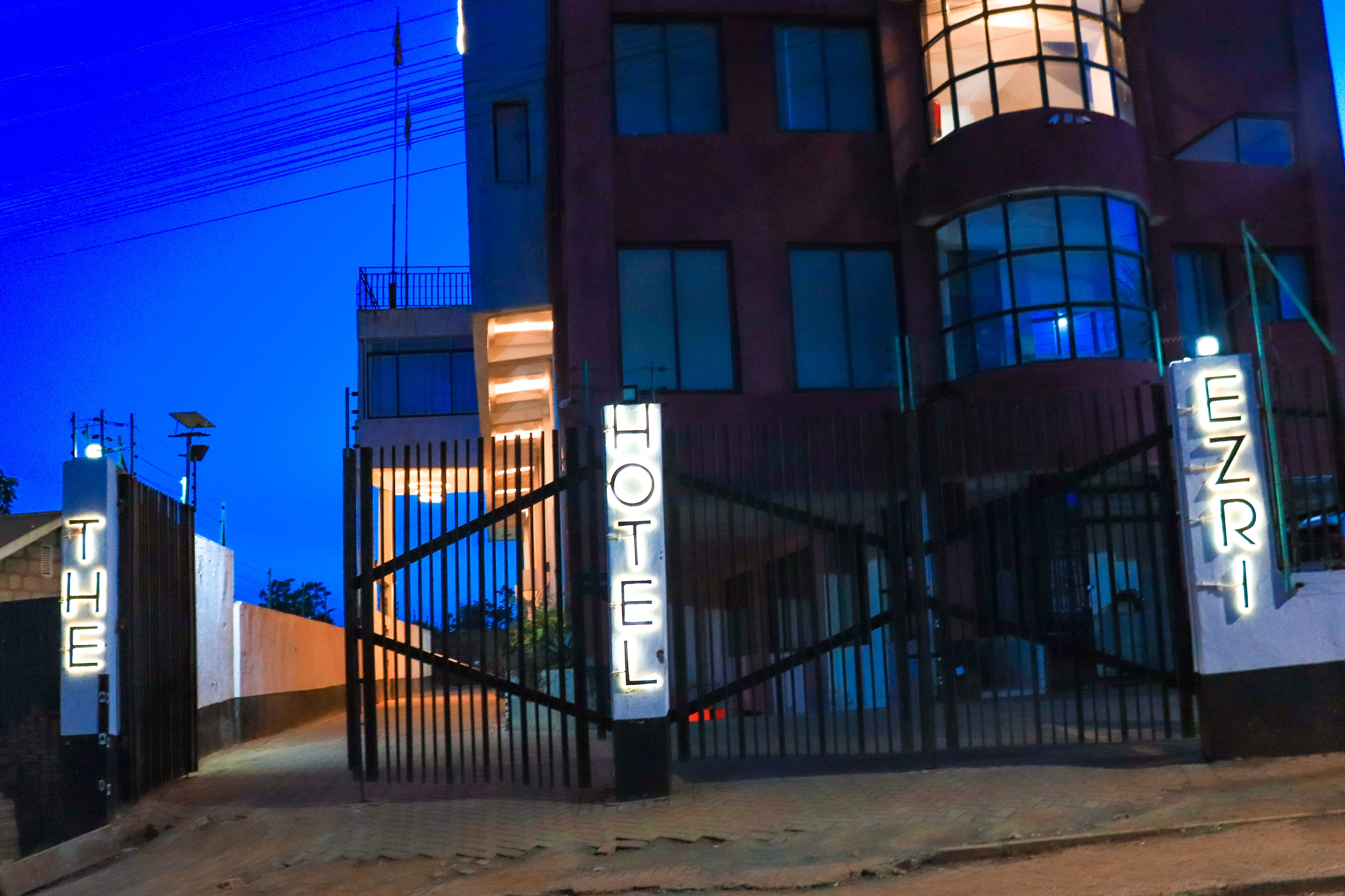 L'ingresso di un hotel con un viale recintato, una targa che indica il nome dell'hotel e un edificio con numerose finestre e balconi.