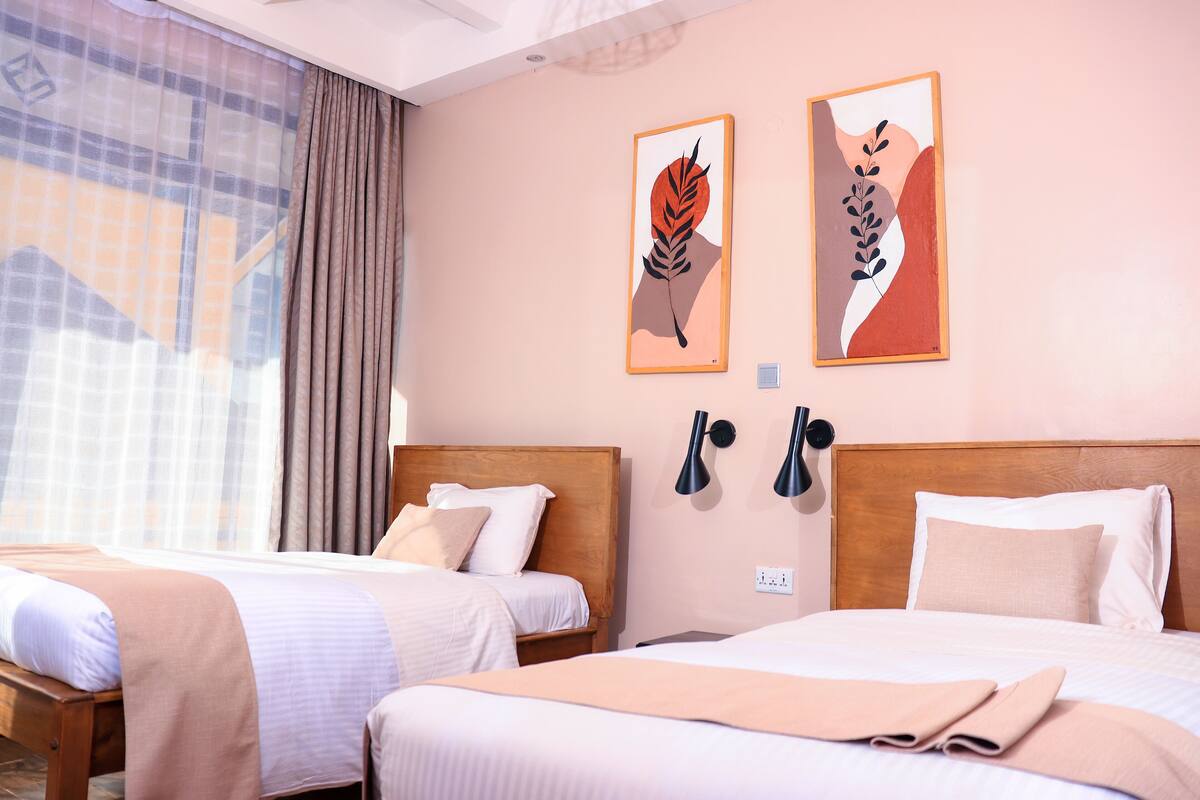 A hotel room with two beds, a large window with curtains, and two wall-mounted lamps.