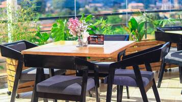 Una mesa con sillas, un jarrón con flores y un cartel de menú en un restaurante con vistas a zonas verdes y edificios.