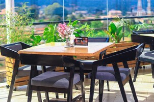 Una mesa con sillas, un jarrón con flores y un cartel de menú en un restaurante con vistas a zonas verdes y edificios.