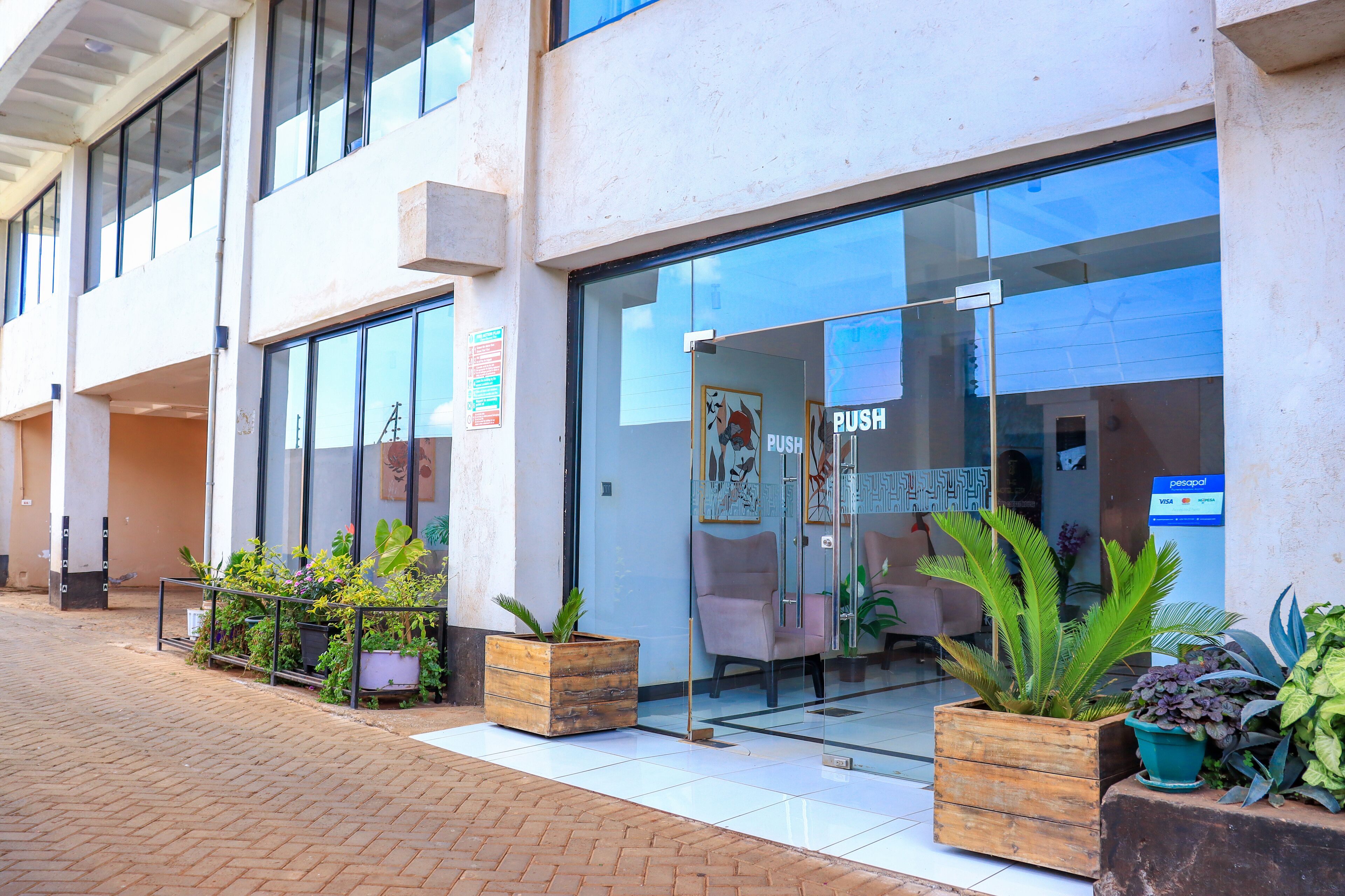 A modern building with large glass windows, a wooden planter with plants, and a sign indicating a push service.