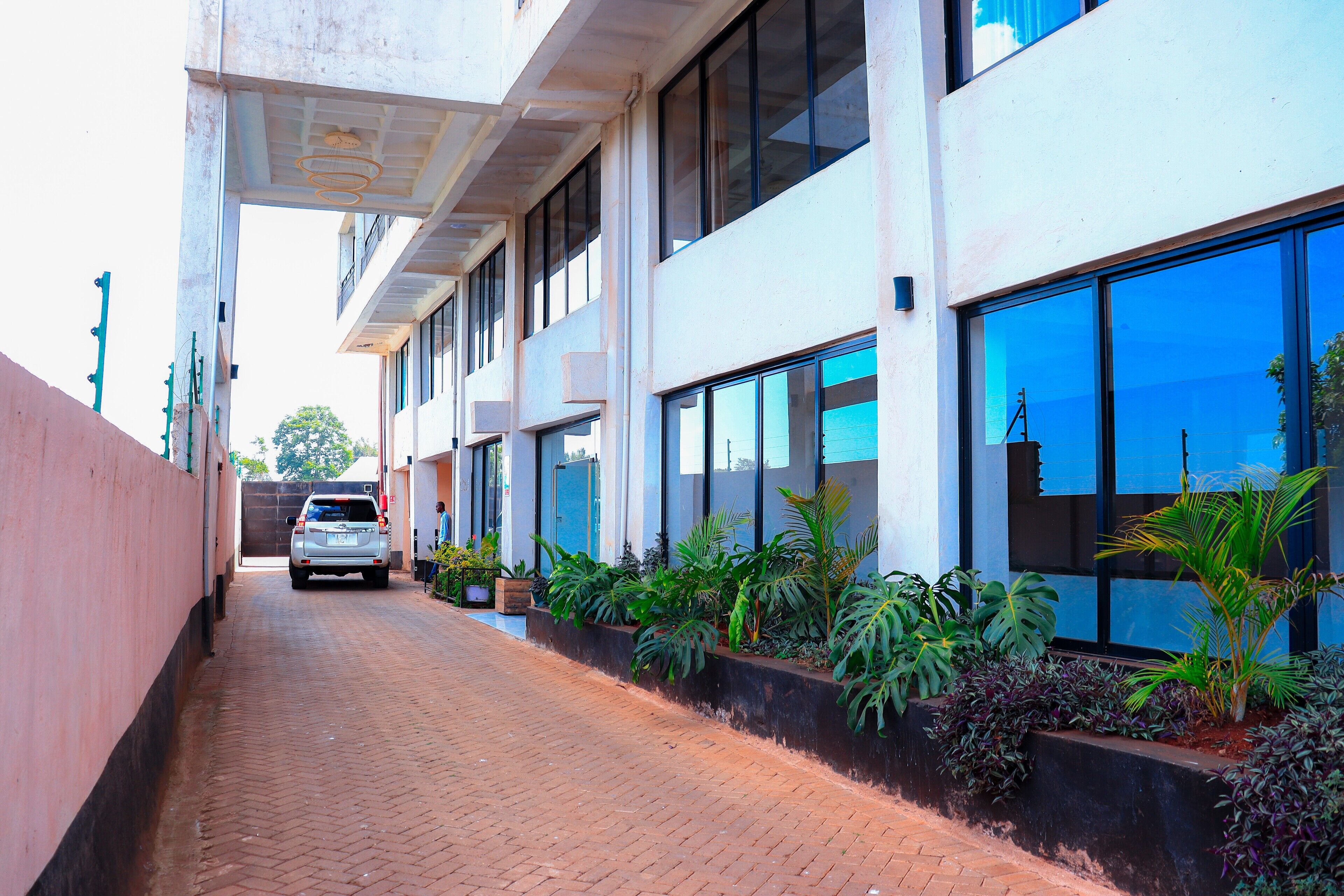 A building with a brick pathway, large windows, and potted plants along the side.