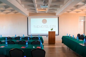 Un salón de conferencias con una larga mesa, sillas, botellas de agua y un atril.