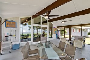 A spacious indoor area with a glass table and chairs, ceiling fans, and a view of the outdoors. - Quaint waterfront home with private beach (Montross)