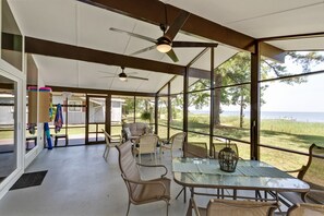 An open-plan living area with a glass table, wicker chairs, ceiling fans, and a view of the outdoors. - Quaint waterfront home with private beach (Montross)