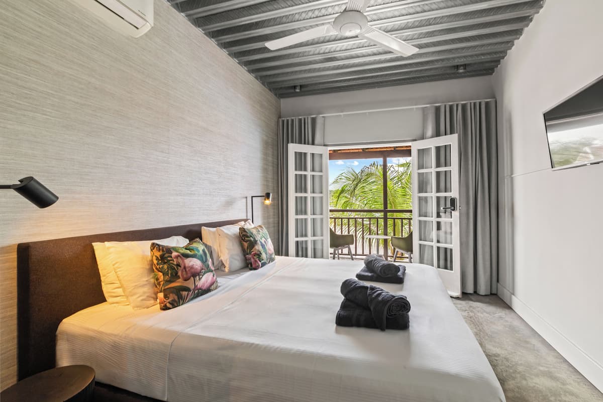 Ein modernes Hotelzimmer mit einem großen Bett, einem Deckenventilator und einem Balkon mit Vorhängen.