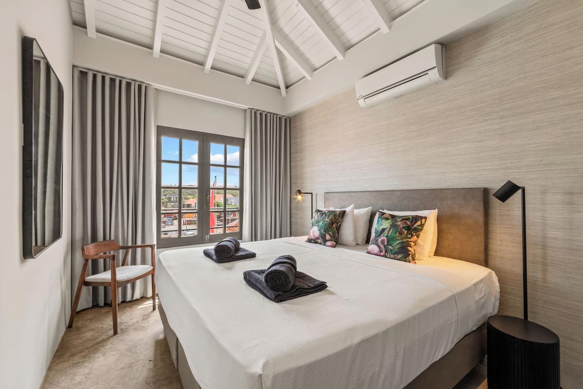 Ein modernes Hotelzimmer mit einem großen Bett, einem Sessel und Blick auf die Stadt durch das Fenster.
